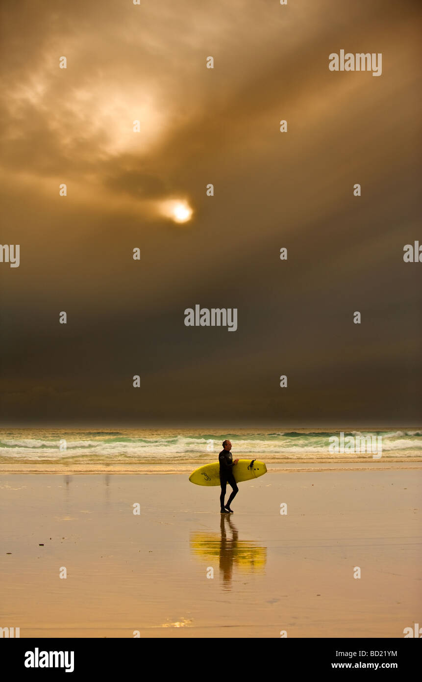 Ein Surfer, zu Fuß am Strand bei Sonnenuntergang. Stockfoto
