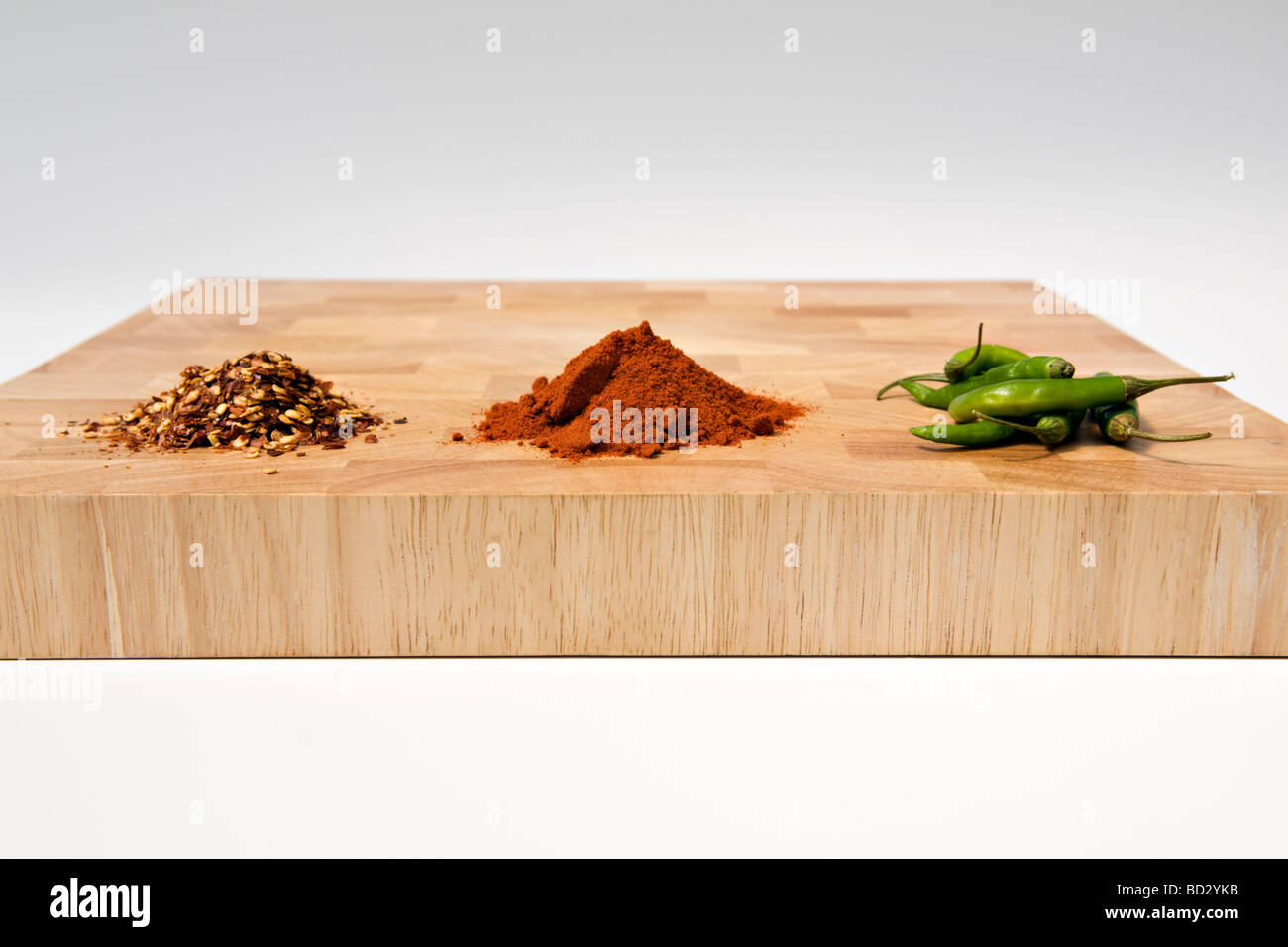 Auswahl an Chili, getrocknet, pulverisiert und frisch, auf hölzernen Schneidebrett vor weißem Hintergrund Stockfoto