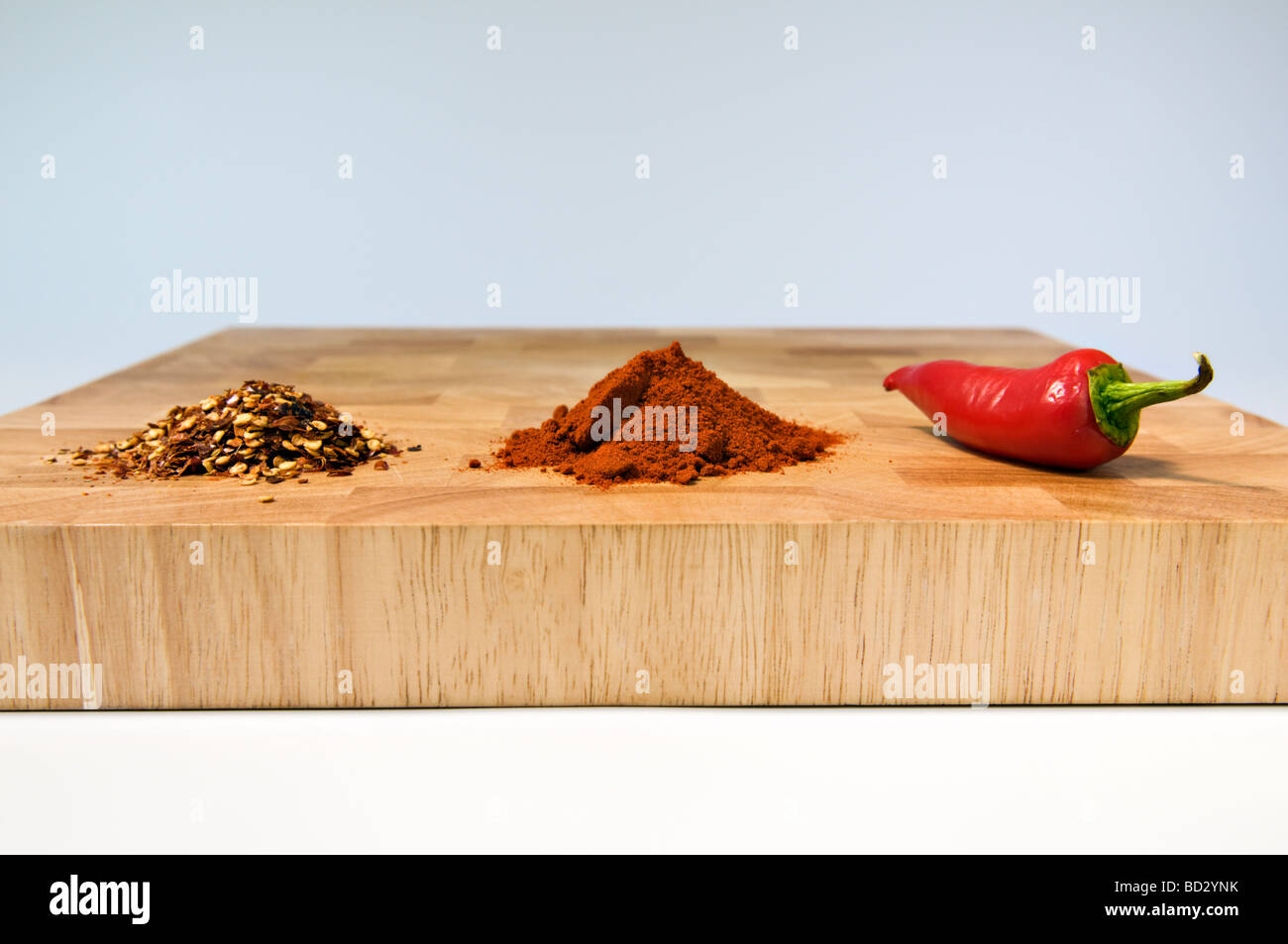 Auswahl an Chili, getrocknet, pulverisiert und frisch, auf Schneidbrett aus Holz Stockfoto