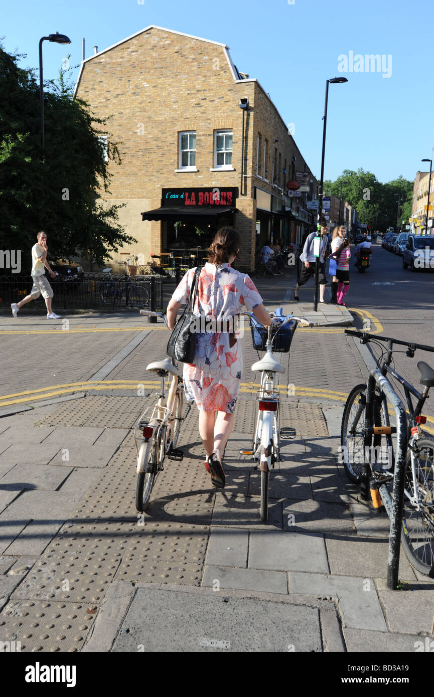 Frau zu Fuß 2 Fahrräder auf Broadway Market Hackney London Stockfoto