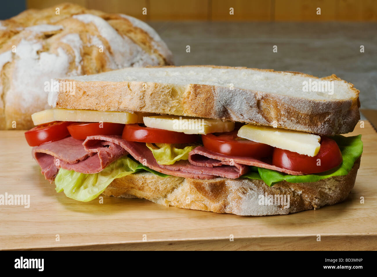 Ein Französisch Boule-Weißbrot-Sandwich mit einer Füllung aus Kopfsalat Pastrami Cheddar Käse und Tomaten Scheiben Stockfoto