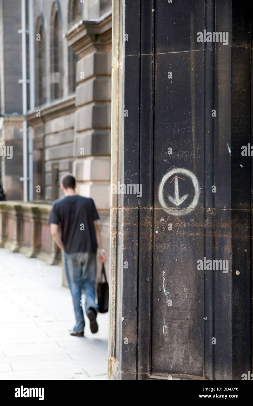 Eine Säule auf Teviot Place, Edinburgh mit Graffiti und Kreis mit einem nach unten Pfeil. Ein Mann geht vorbei im Hintergrund Stockfoto