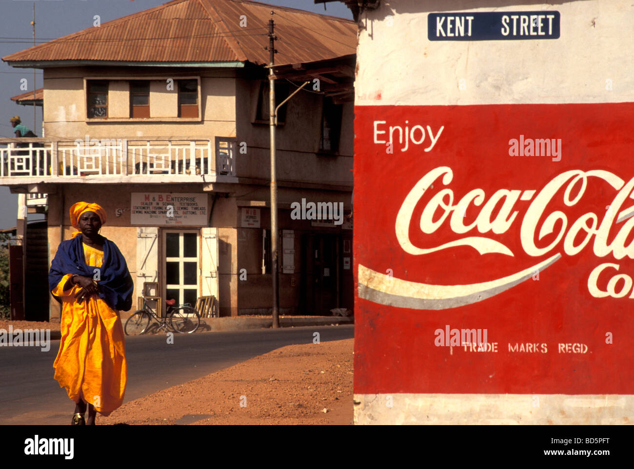 Frau in einer Straße mit Cocoa Cola Werbung in Banjul Gambia Stockfoto