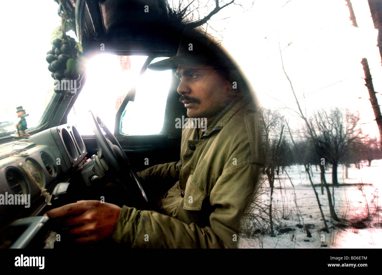 Ein indischer Soldat hört Radio in seinem Fahrzeug wie der Schnee bedeckte Landschaft auf einer Straße in im Fenster reflektiert wird Stockfoto