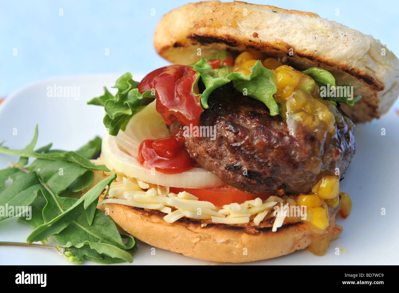 Burger in Brötchen mit Käse Zwiebel Mais Relish und Salat Stockfoto