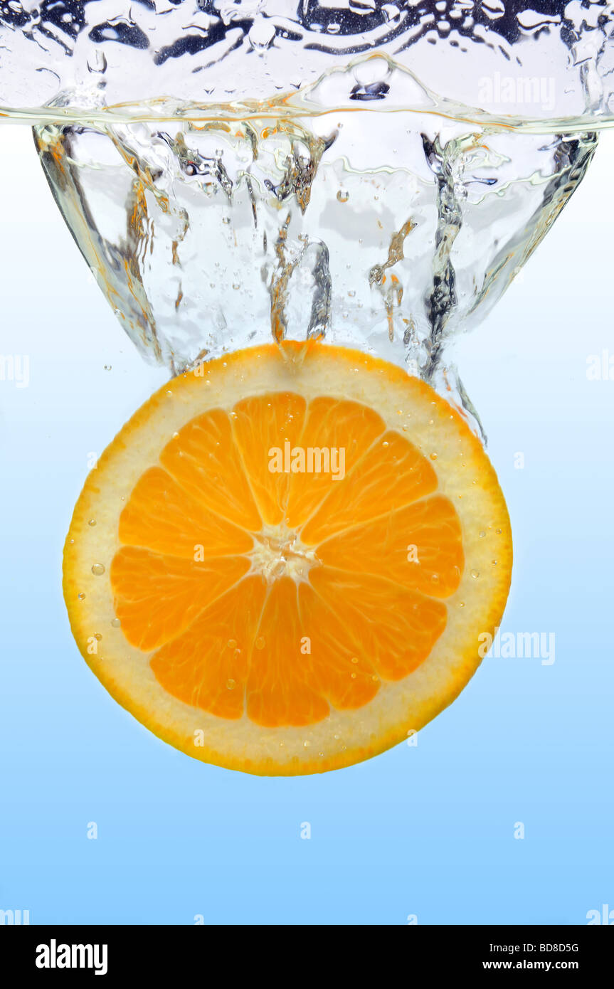 Orangenscheibe spritzt ins Wasser über hellblauen Hintergrund Stockfoto