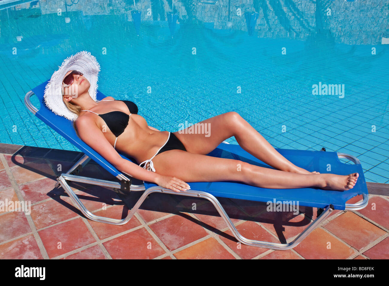 Junge weiße, blonde Frau auf blaue Sonnenliege am Pool liegend Stockfoto