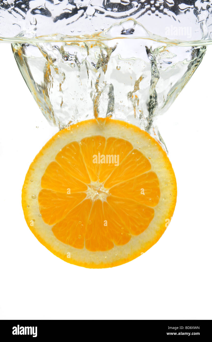 Orangenscheibe spritzt ins Wasser über weißem Hintergrund Stockfoto