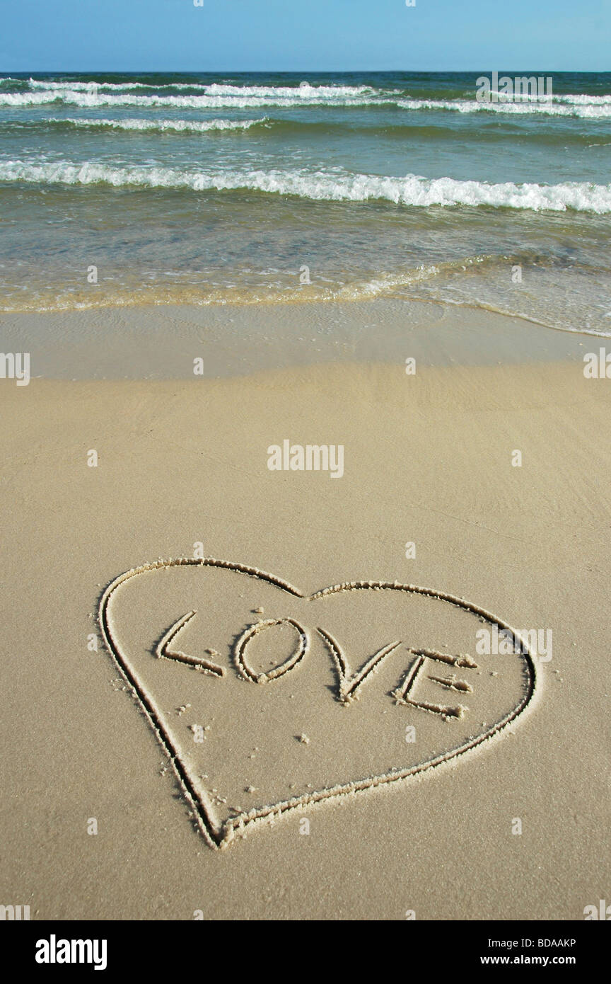 Herz und Liebe geschrieben am Ufer mit Wellen im Hintergrund Stockfoto