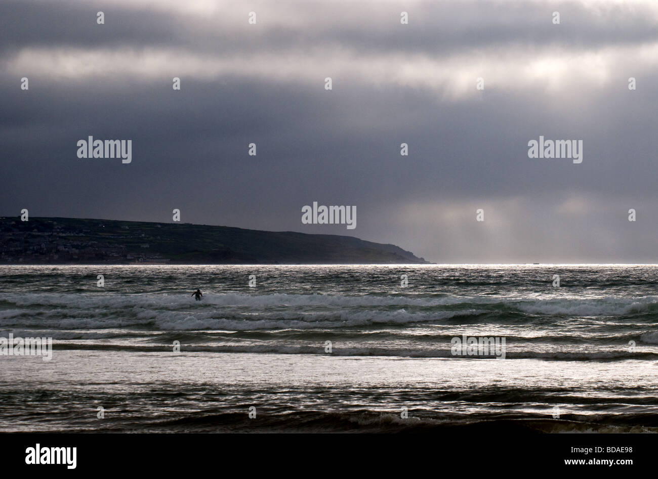 Regenwolken sammeln über ein einsamer Surfer in St Ives Bay in Cornwall.  Foto von Gordon Scammell Stockfoto