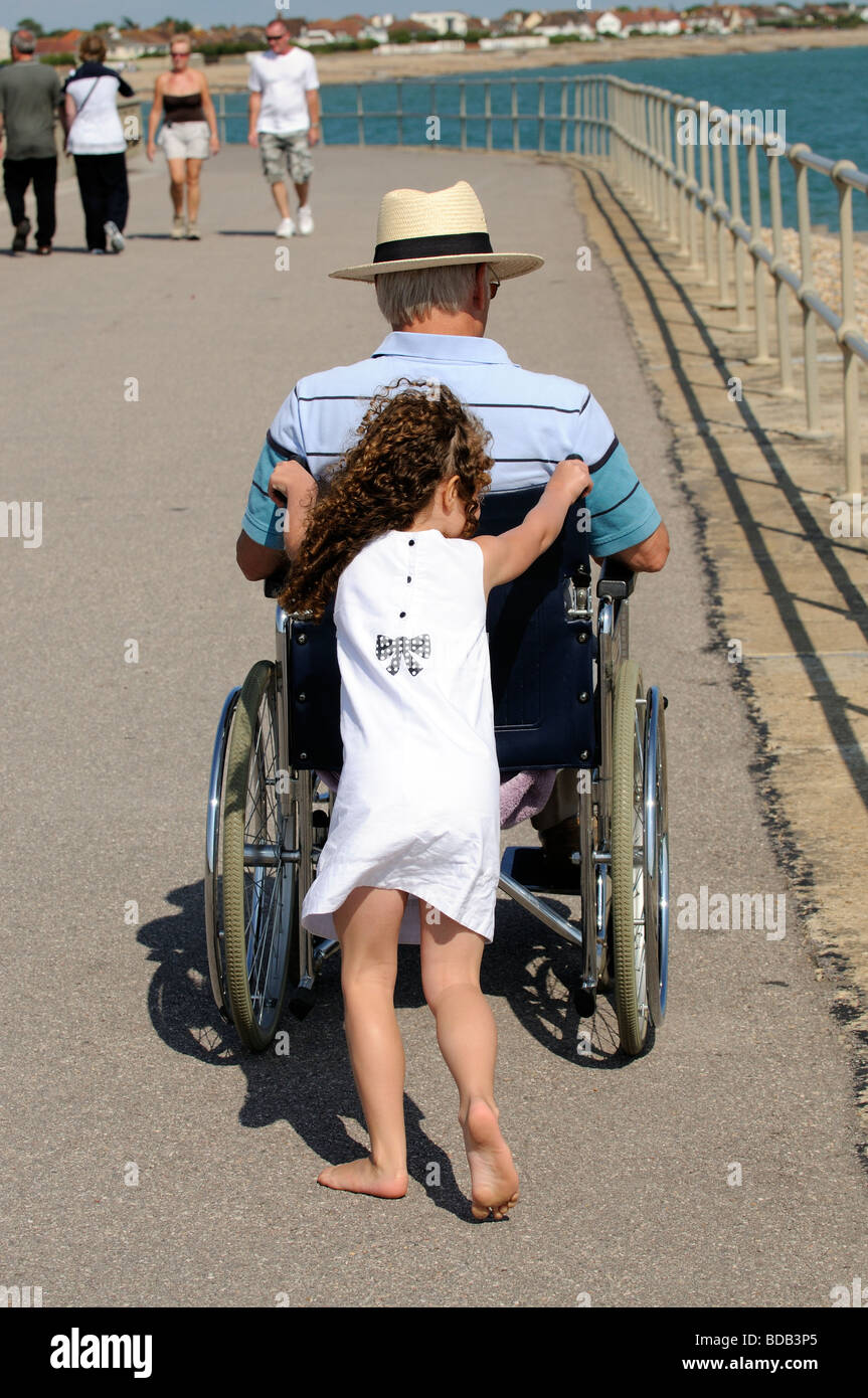 Kleines Mädchen schob eine Erwachsene Rollstuhlfahrer entlang der Abschlussball in Bognor Regis England UK Stockfoto
