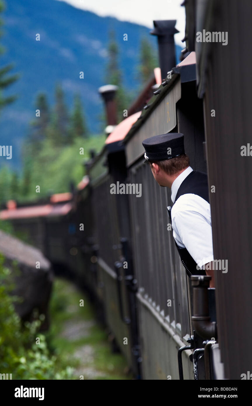 Skagway, Alaska, die Bremse Dirigent auf der White Pass and Yukon Route Railway lehnt sich zwischen Autos für eine bessere Sicht. Stockfoto