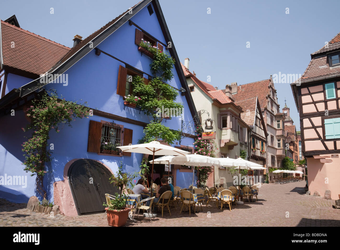 A la Couronne Restaurant in einem alten Gebäude auf schmalen gepflasterten Straße mit Menschen Essen außerhalb im malerischen Dorf. Riquewihr Elsass Haut Rhin Frankreich Stockfoto