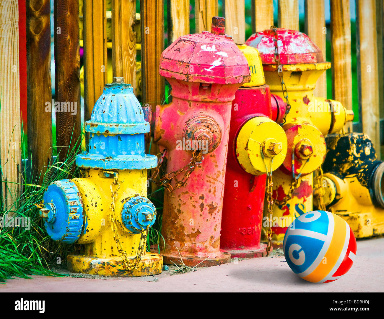 Bunte alte Hydranten bunt bemalt, sitzen auf Bürgersteig gegen Holzzaun und des Kindes Gummiball. Stockfoto