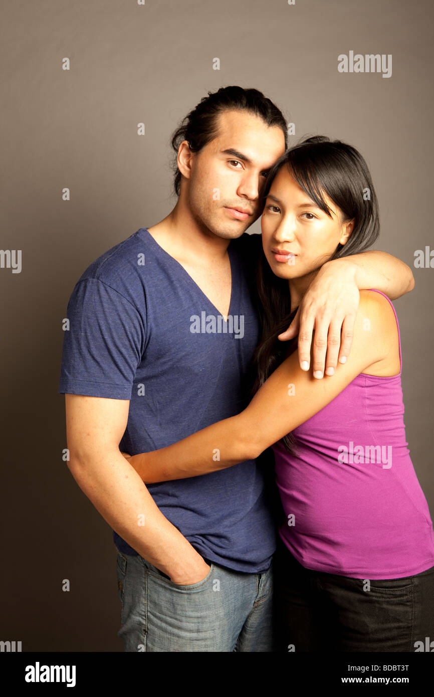 Porträt der philippinischen Frauen und ethnische männlichen Partner halten einander vor grauem Hintergrund.  Blick in die Kamera. Stockfoto