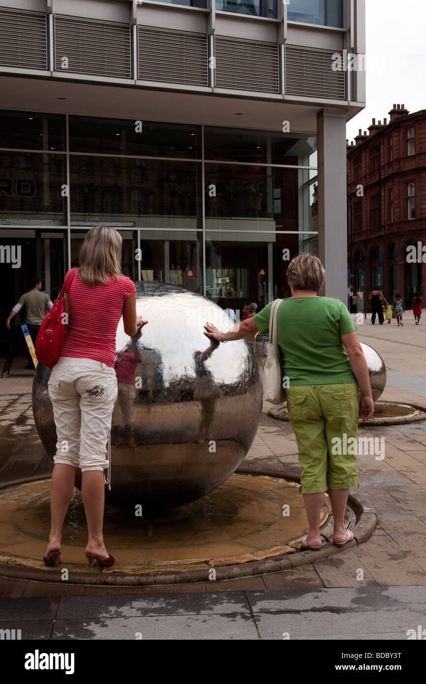 Frauen berühren das Wasser fließt über eines der Stahlkugeln in Sheffield Millenniums-Gärten Stockfoto