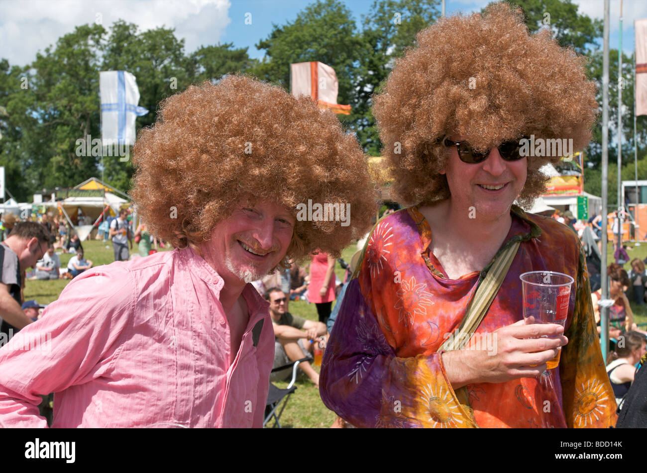 Hippy Shirts und Afro Perücken von zwei Männern wie Fancy Dress bei Musikfestivals WOMAD getragen genießen Sie ein Bier in der Sonne Stockfoto Hippy Shirts und Afro Perücken von zwei Männern wie Fancy Dress bei Musikfestivals WOMAD getragen genießen Sie ein Bier in der Sonne Stockfoto