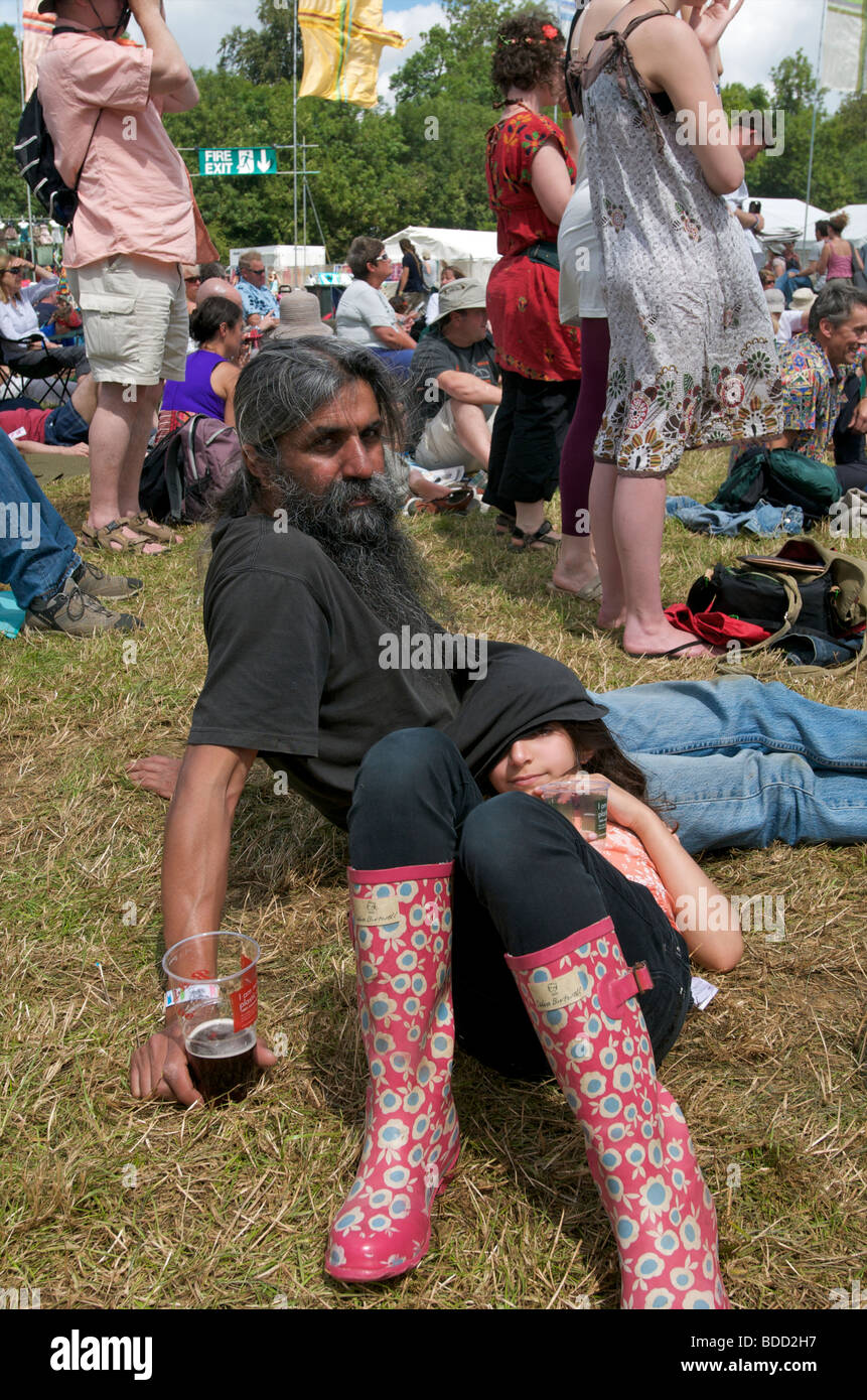 Ein Vater und eine Tochter liegen auf dem Gras, umgeben von Menschenmassen beim WOMAD Musikfestival Stockfoto