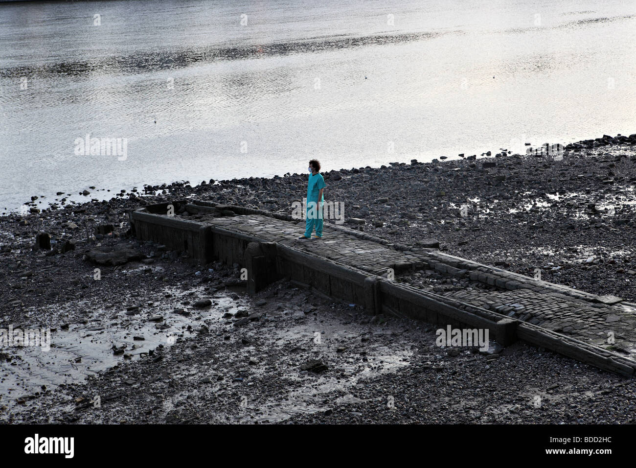 Ein Mann starrt auf der Themse von seiner Bank. Er trägt eine chirurgische Uniform und Gesichtsmaske. Stockfoto