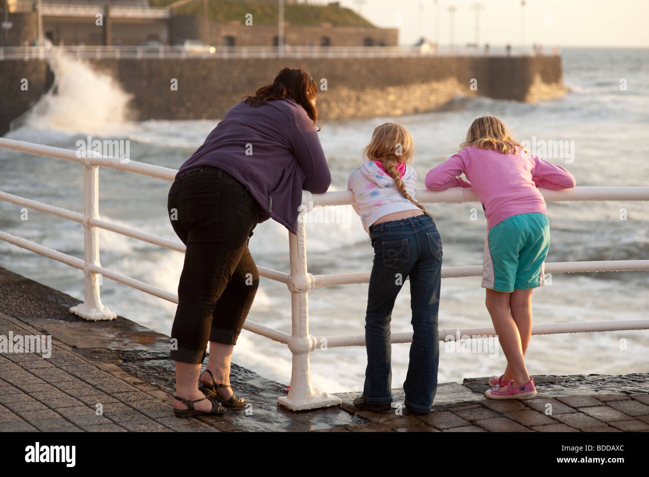eine Mutter und ihren beiden Töchtern beobachten die Wellen gegen die Promenade, Aberystwyth Wales UK Stockfoto
