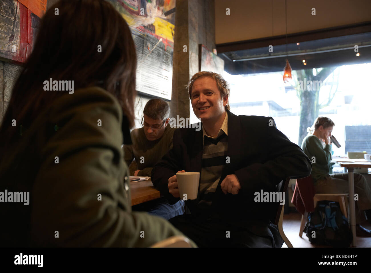 Gäste sitzen und plaudern, trinken warme Getränke im Café. Stockfoto