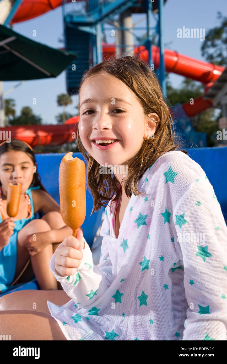 Junges Mädchen essen Corndog im Wasserpark im Sommer Stockfoto