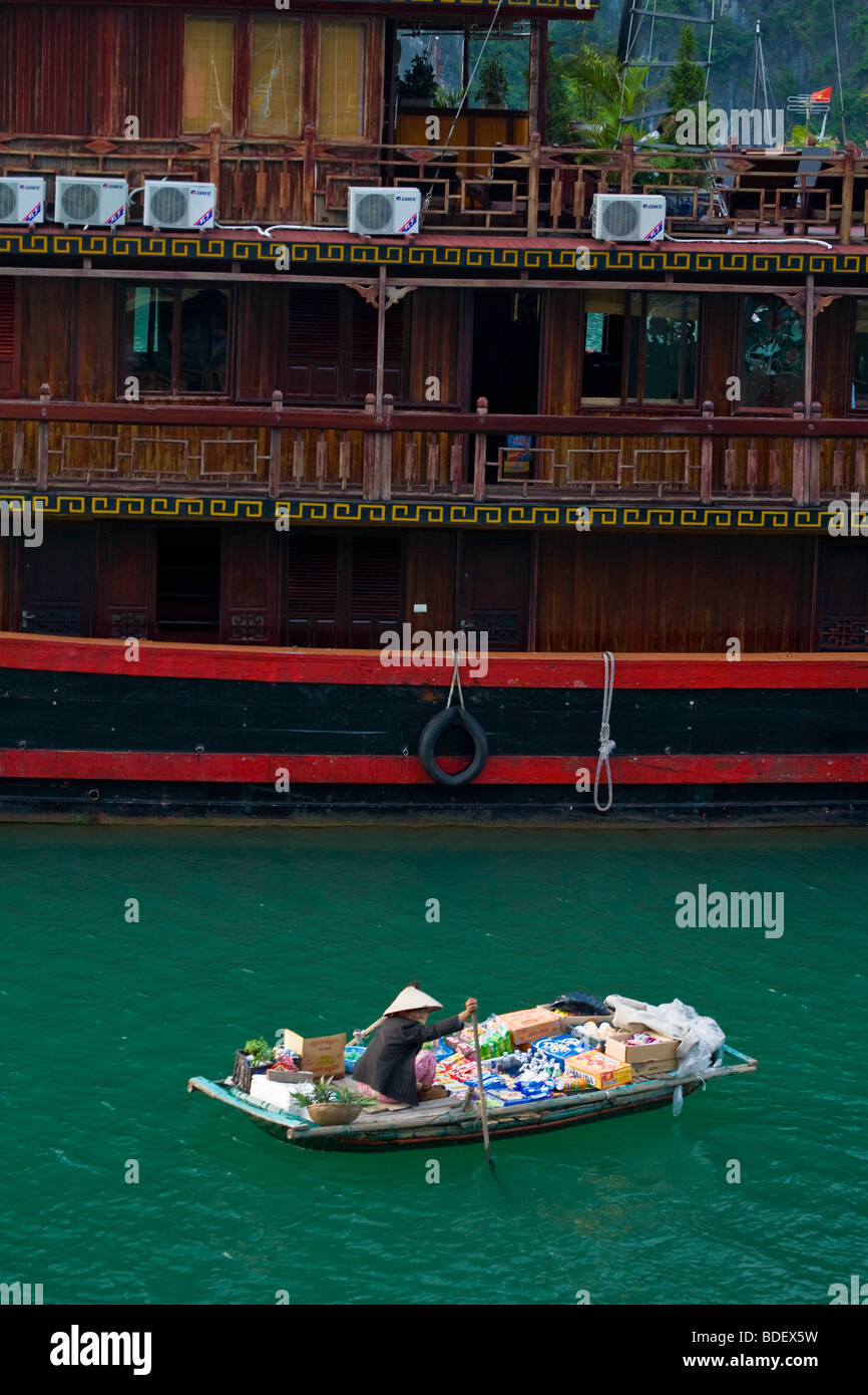 Eine Frau in einem kleinen Boot bewegt sich zwischen großen touristischen Boote, Süßigkeiten zu verkaufen und Snacks in Ha Long Bucht, Vietnam Stockfoto
