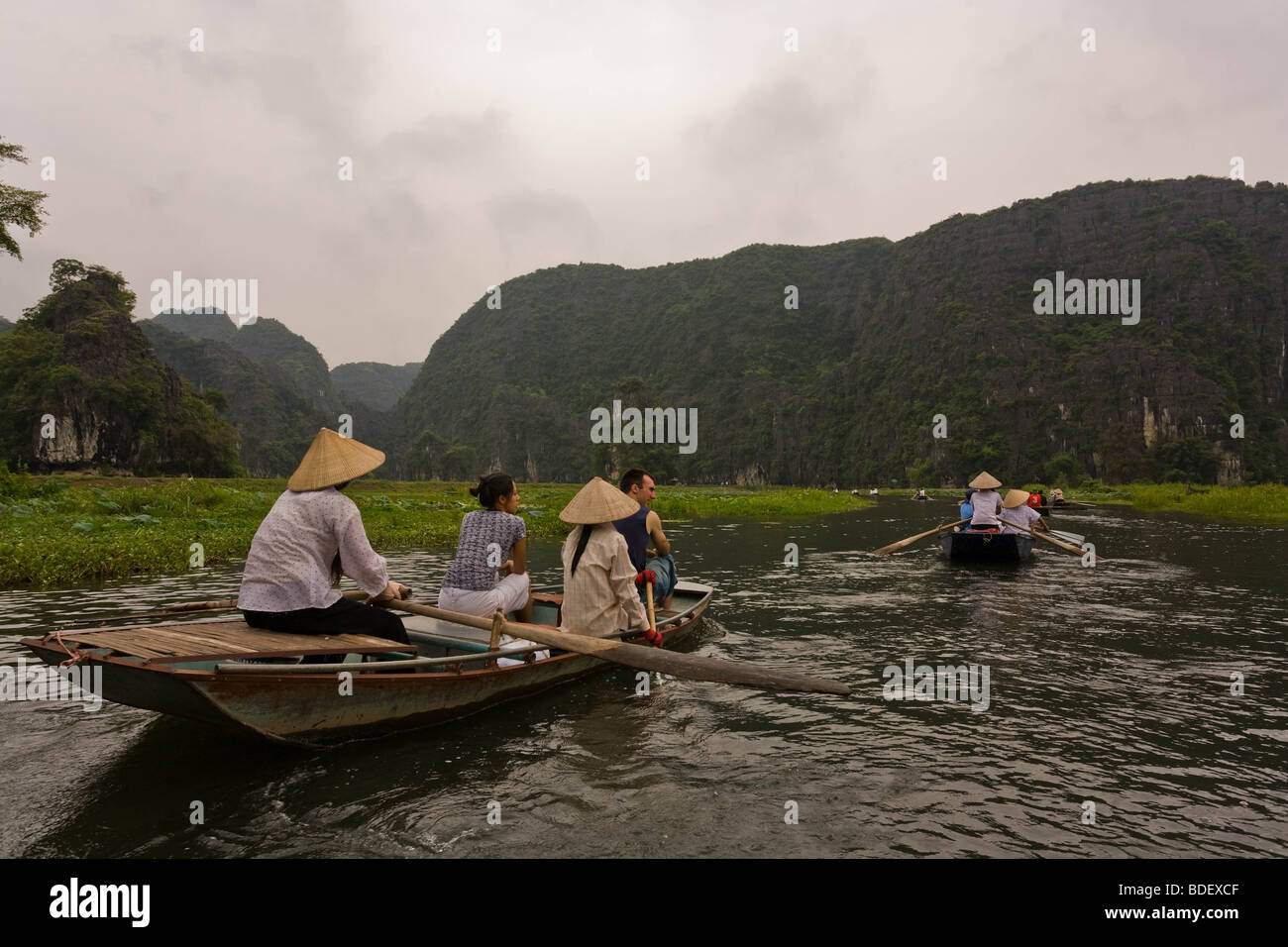 Einheimische Frauen lenken kleine Boote entlang der Wasserstraßen zwischen massiven Kalkstein-Klippen, Hoa Binh, Vietnam Stockfoto