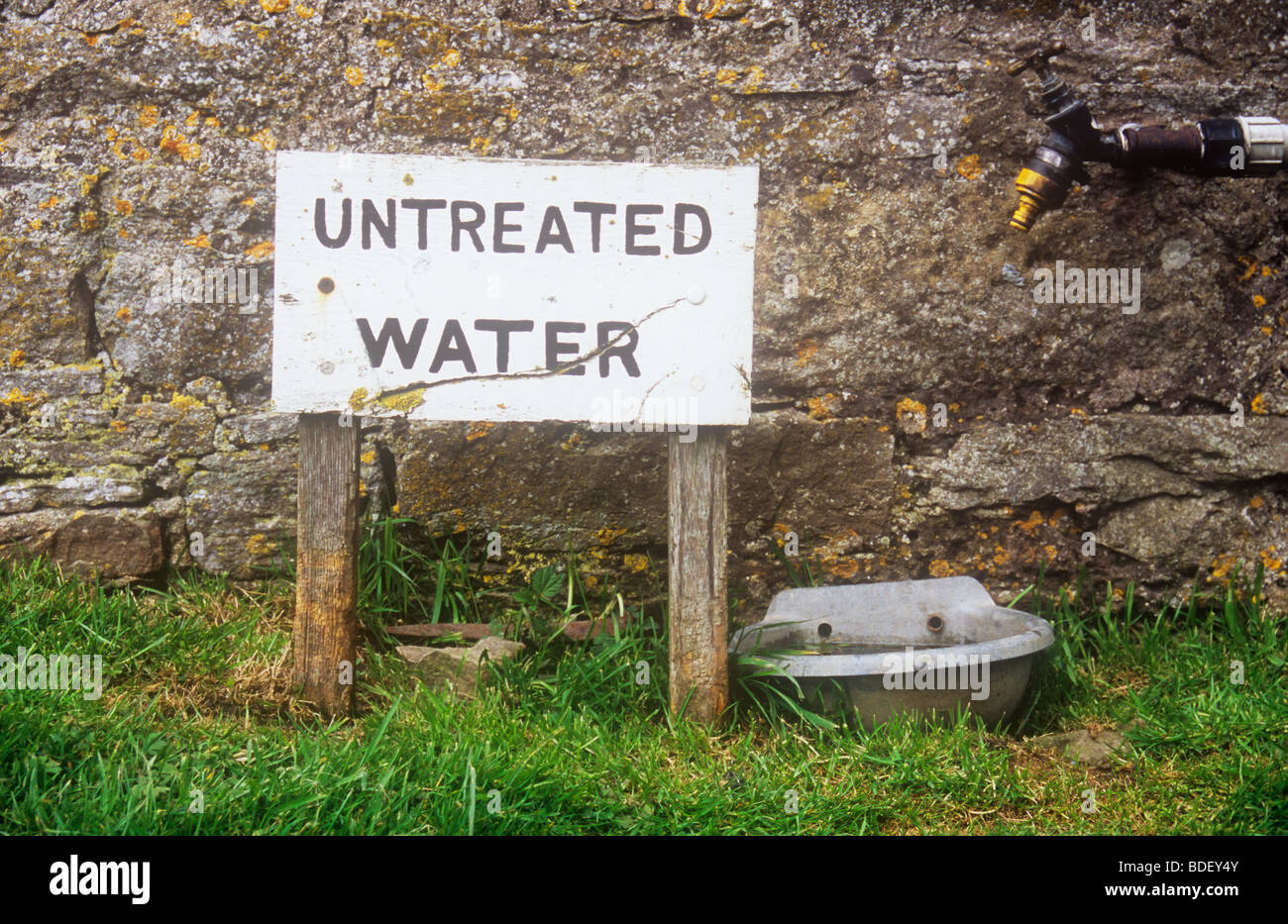 Zeichen vor der Steinmauer neben großen Wassernapf und unter Angabe von unbehandeltem Wasser Wasserhahn Stockfoto