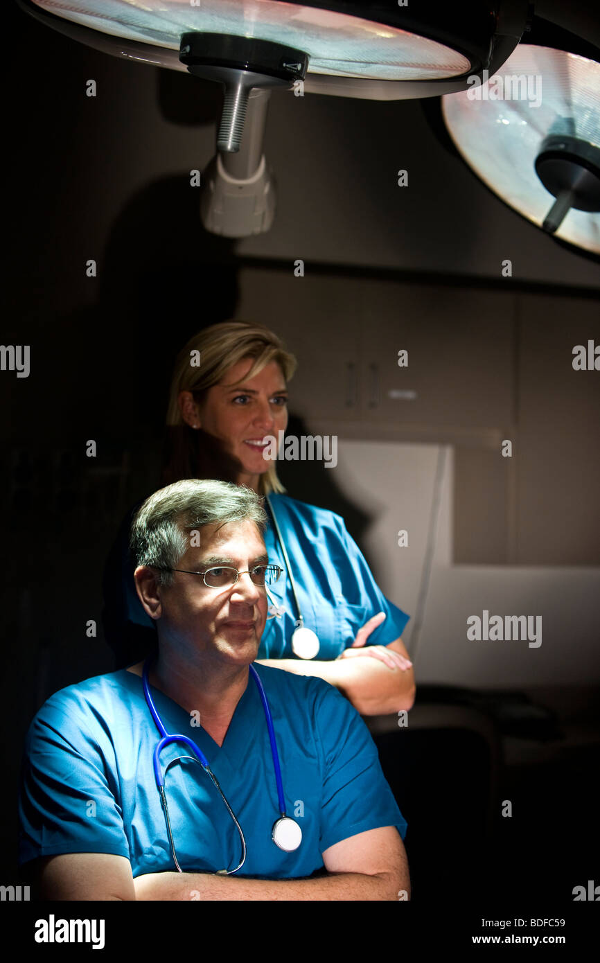 Porträt von Ärzten in Scrubs stehend im Krankenzimmer mit OP-Leuchten Stockfoto