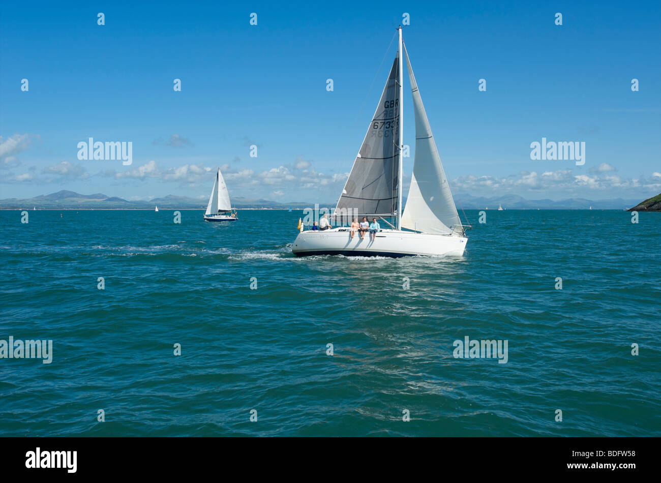 Segelyacht in Abersoch Bay North Wales mit der Crew an einem sonnigen Tag mit den Beinen über der Seite Stockfoto