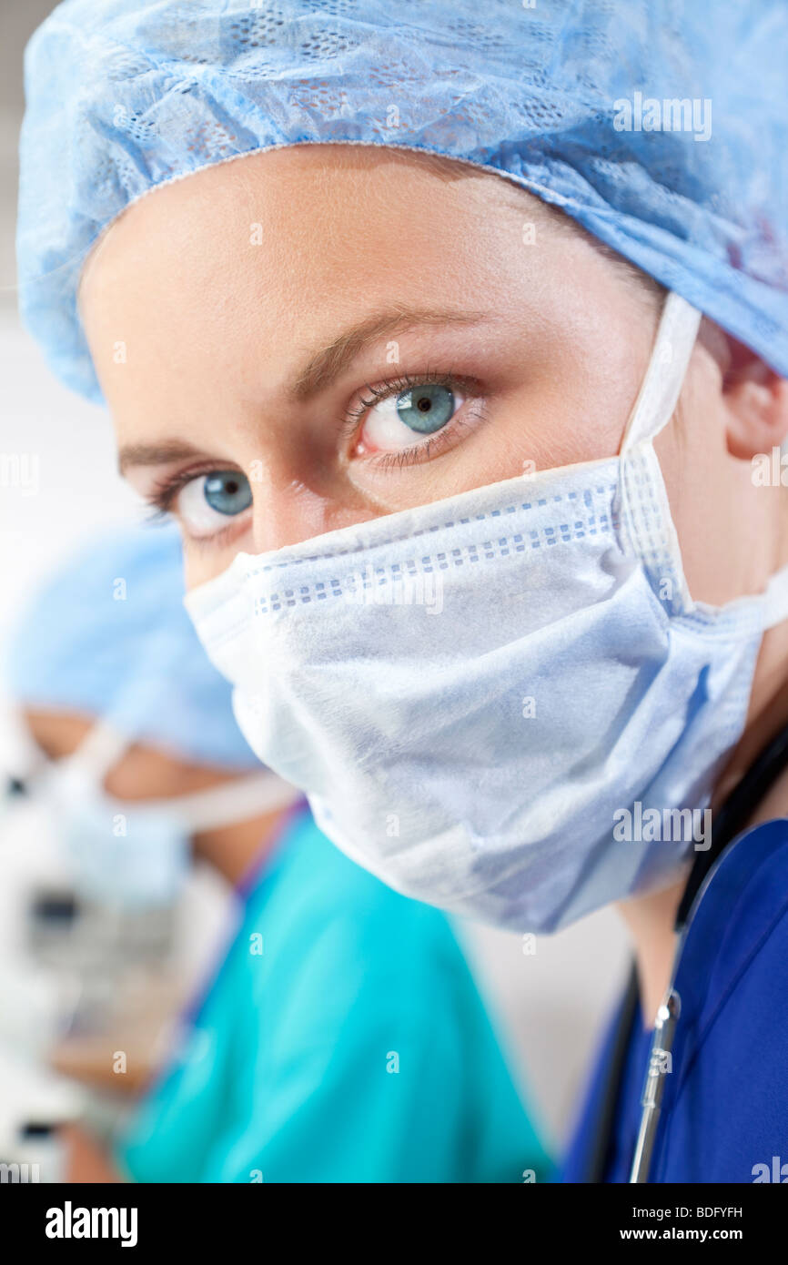 Eine schöne Ärztin in chirurgischen Peelings erschossen in einem Krankenhaus mit ihrer Kollegin unscharf hinter ihr. Stockfoto