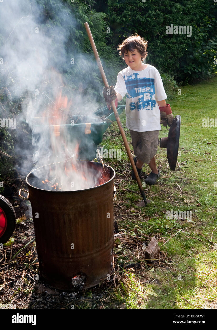 Jungen im Alter von sieben brennende Gartenabfälle im Verbrennungsofen mit Rauchschwaden. Stockfoto