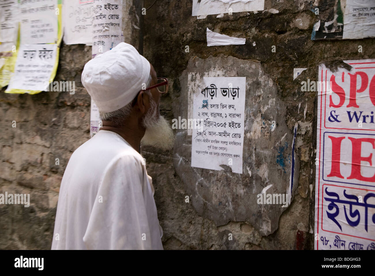 Ein Mann liest eine Mitteilung über eine Mauer außerhalb in Bangladesch Stockfoto