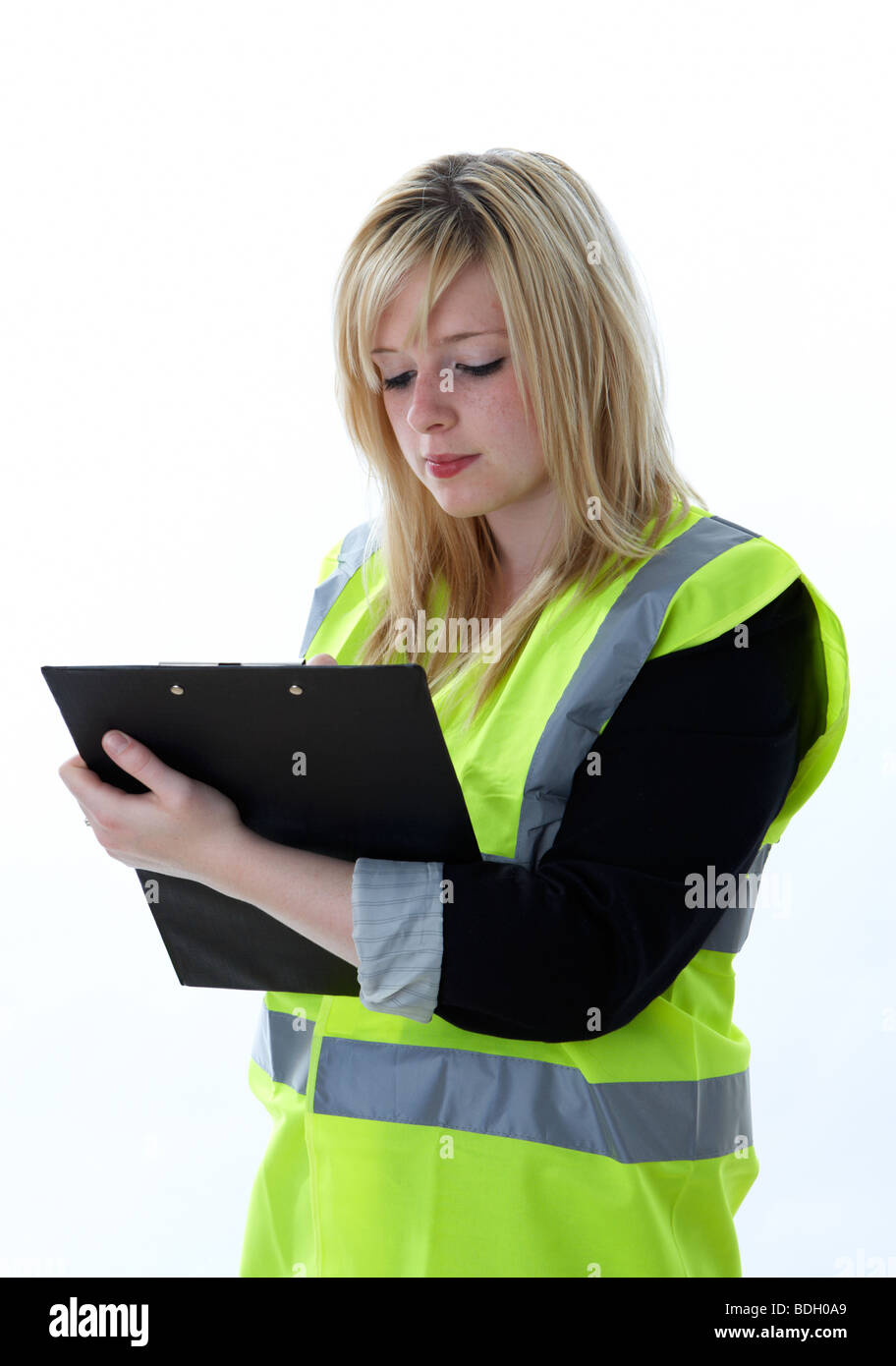 junge 20 jährige blonde Frau mit einem hohen Vis Weste konzentriert sich schriftlich auf einem Klemmbrett Stockfoto