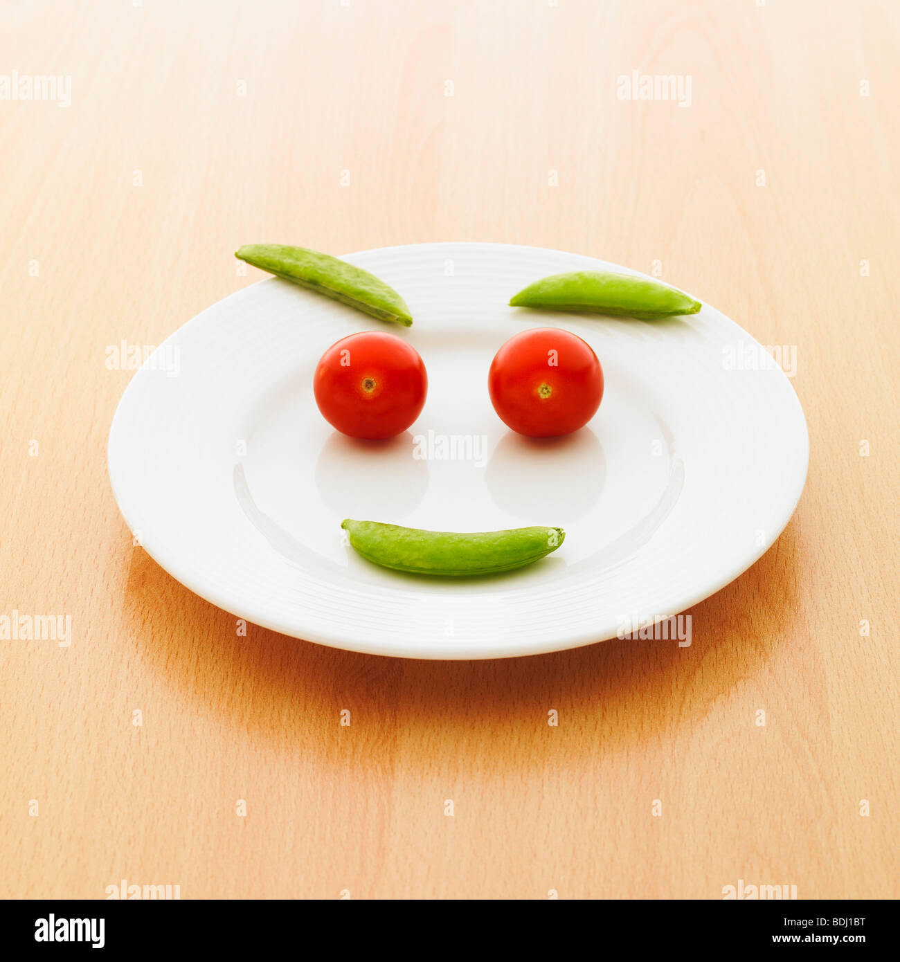 Ein Teller mit Kirschtomaten und Zuckerschoten machen ein Smiley-Gesicht. Stockfoto