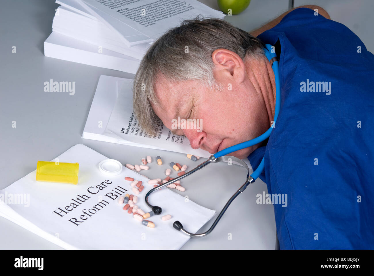 Ein Arzt ist über seinen Schreibtisch nach Überdosierung, sobald er die Gesundheitsreform Rechnung gelesen eingebrochen. Stockfoto