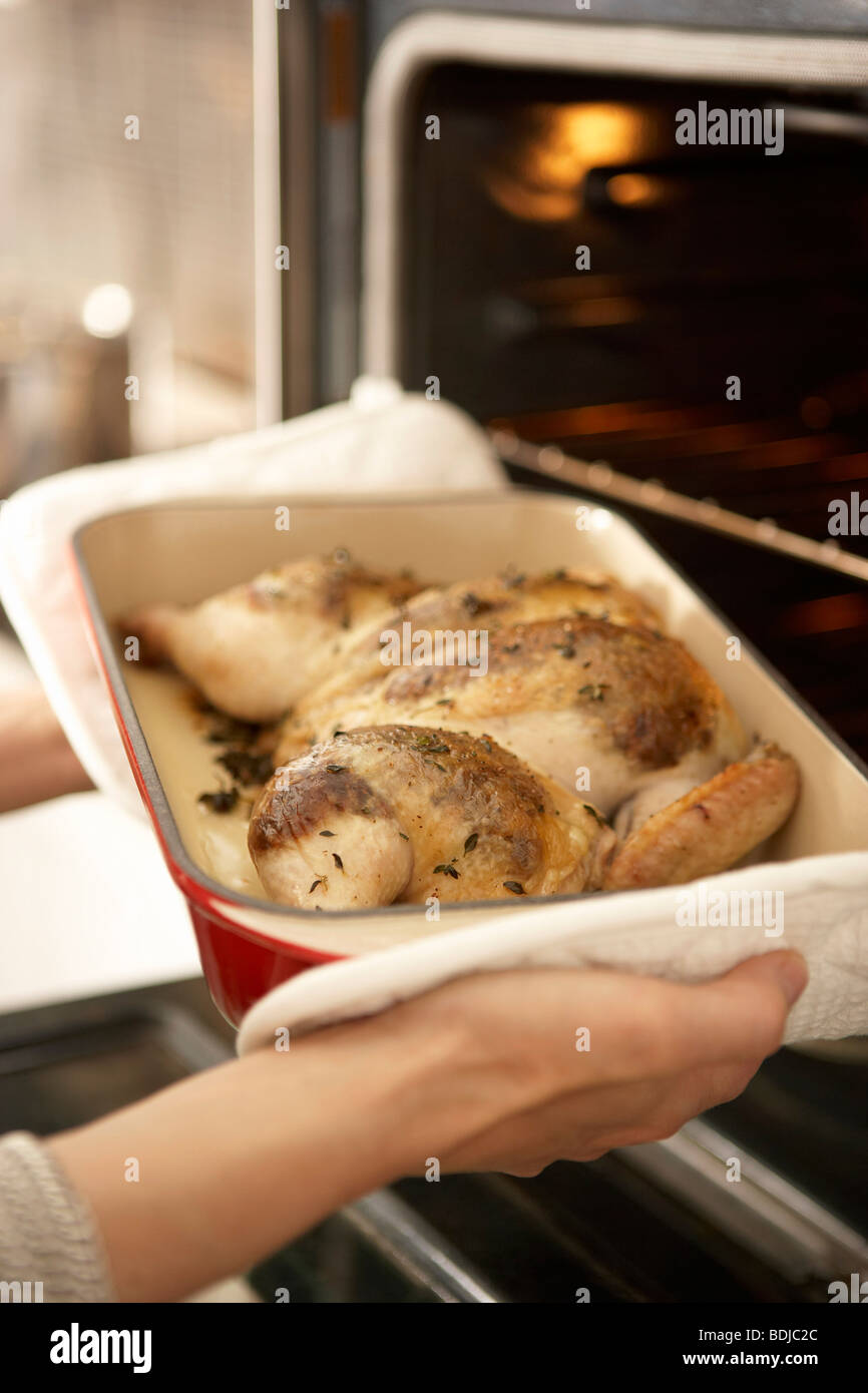Frau nimmt Roast Chicken aus Ofen Stockfoto