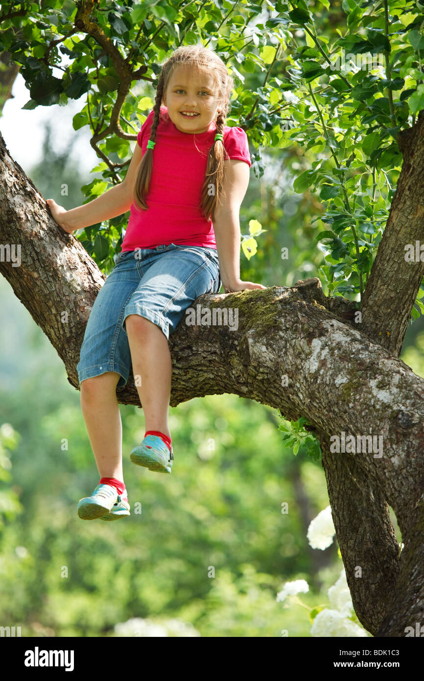 Kleines Mädchen sitzend auf Ast Stockfoto