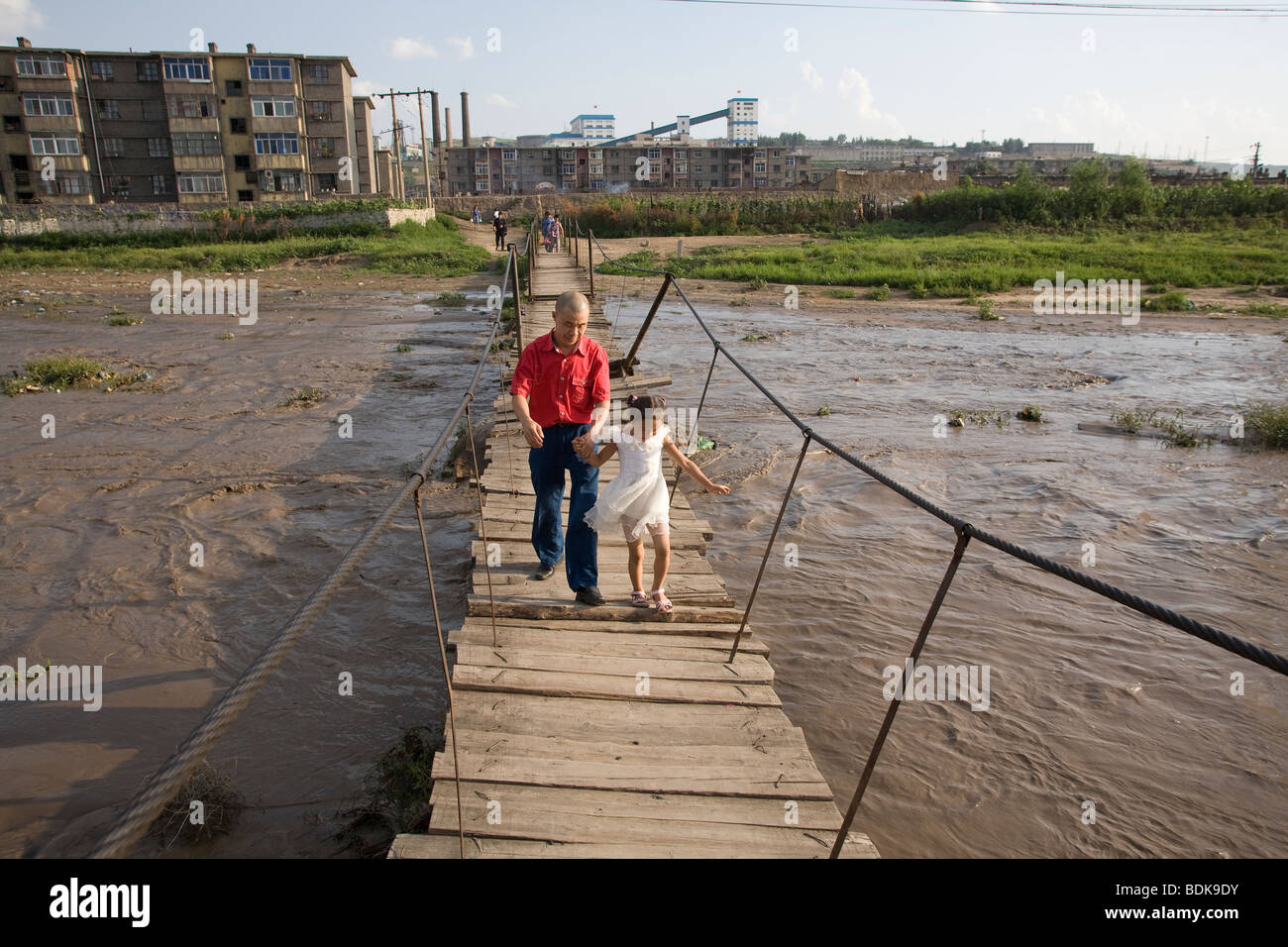 DATONG, Provinz SHANXI, CHINA - AUGUST 2007: Hilft ein Vater seine Tochter auf einem Holzsteg über den Fluss Stockfoto