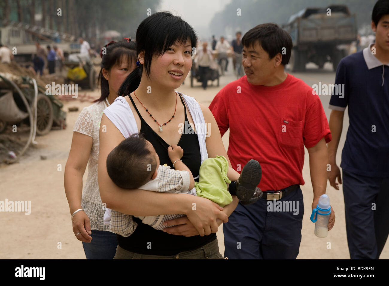 TAIYUAN, Provinz SHANXI, CHINA - August 2007: Eine Frau trägt ihr Baby Sohn auf der Straße. Die Luft ist dick mit Verschmutzung. Stockfoto
