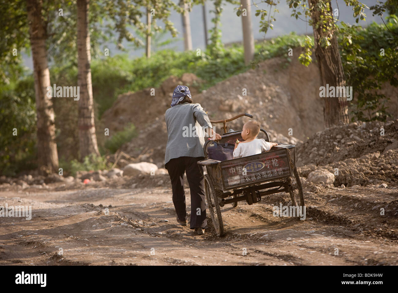 JIEXIU, Provinz SHANXI, CHINA - AUGUST 2007: Eine Mutter schiebt einen Wagen mit ihrem kleinen Sohn auf einem Schotterweg Stockfoto