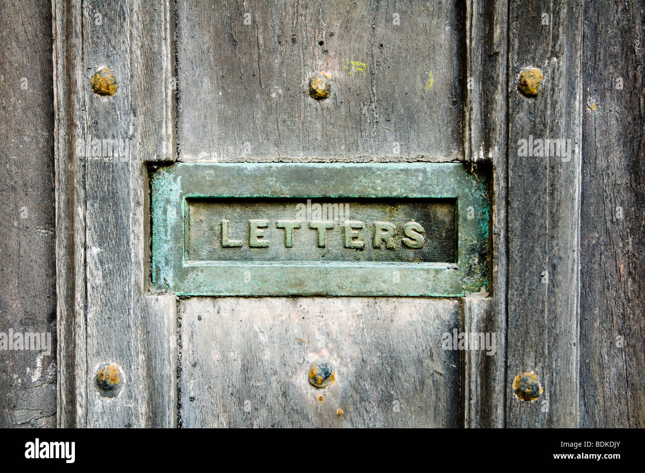 Ein Briefkasten mit Grünspan Patina, eingelassen in eine alte und verwitterte Eichentür mit schweren Nägel. Stockfoto