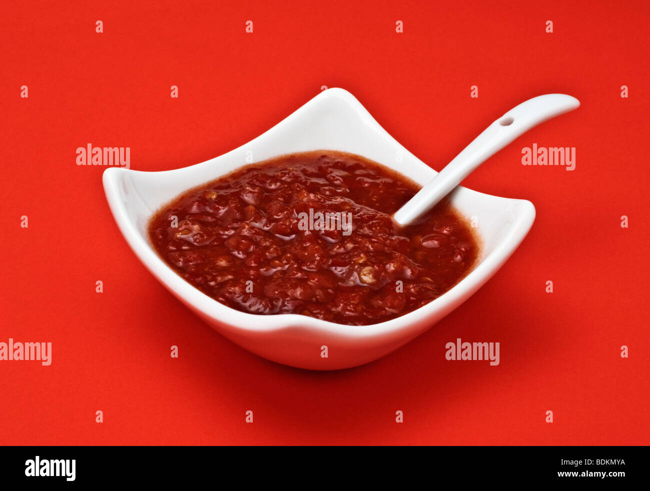 Chilisauce in weißem Gericht mit Servierlöffel auf rotem Grund Stockfoto