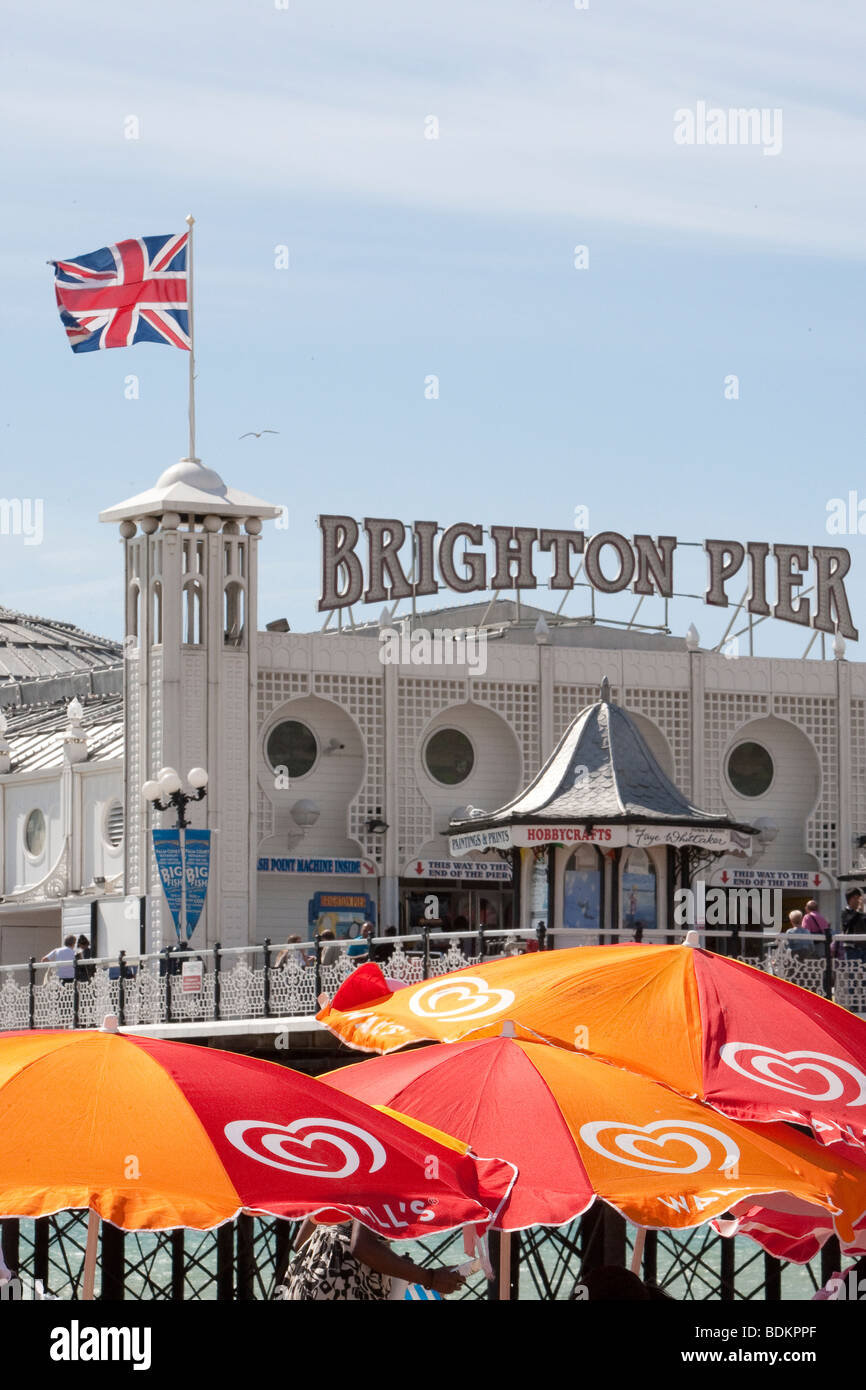 Palace Pier, Fahnen Brighton mit Union Jack in der Sonne fliegen. Bunte Sonnenschirme im Vordergrund. Stockfoto