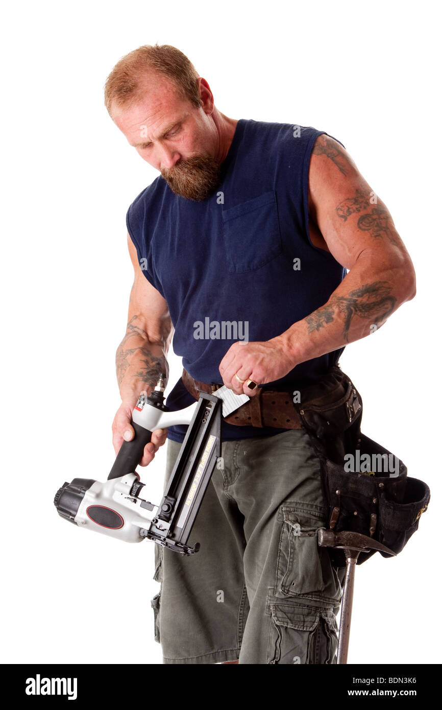 Starker Mann mit Tattoos laden ein Bolzenschußgerät mit Nägeln, tragen ein Werkzeuggürtel mit Hammer, isoliert Stockfoto