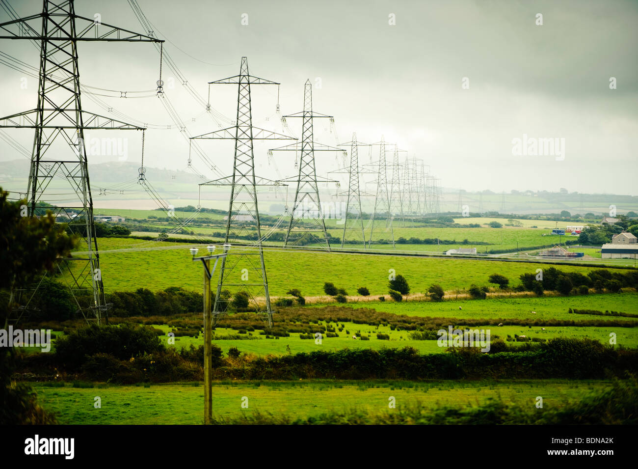 Eine Reihe von nationalen Grid Strommasten marschieren über den ländlichen Landschaft von Anglesey, North Wales, UK Stockfoto