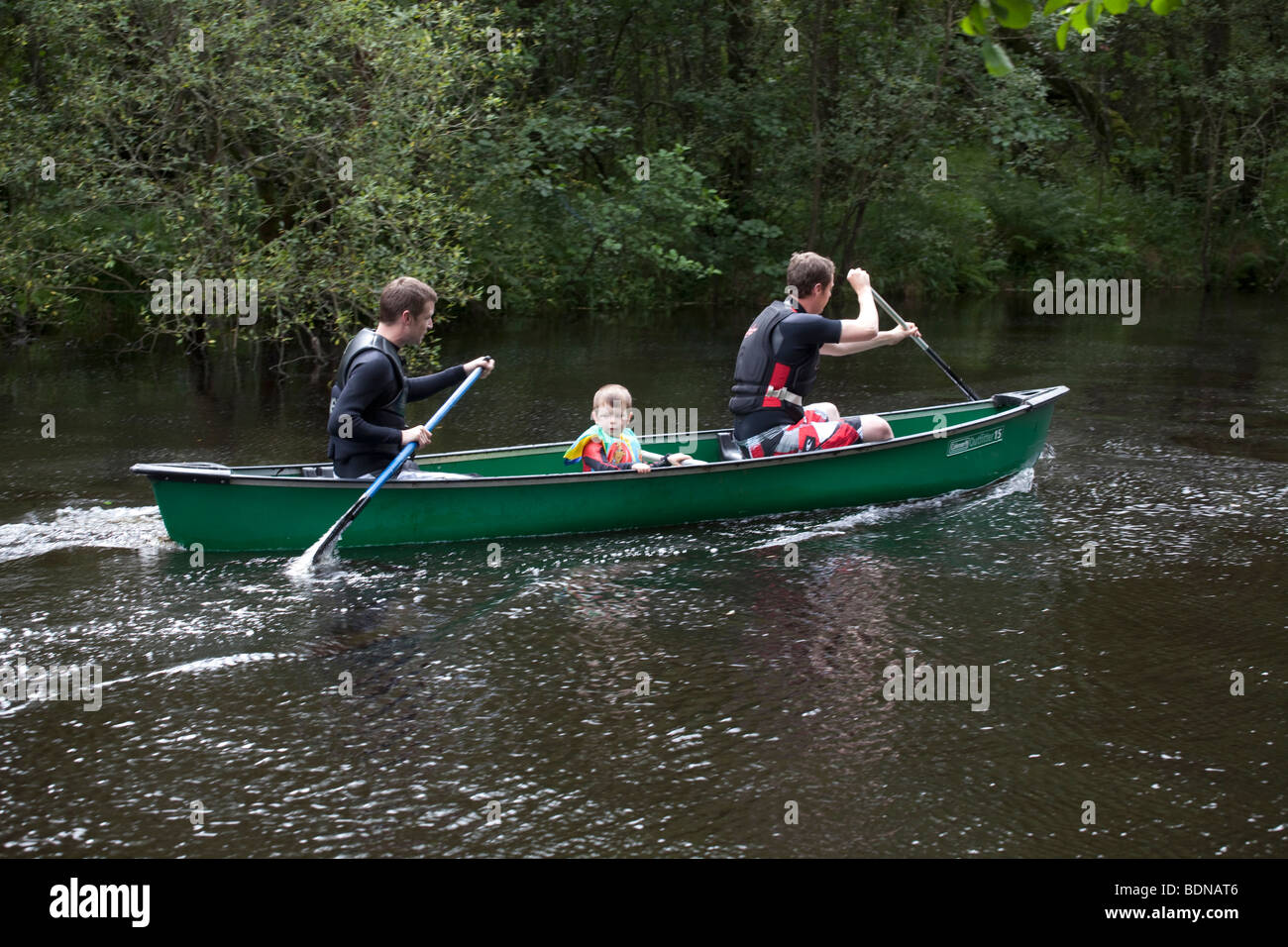 Zwei Männer und ein Junge in einem grünen Kanu an einem Fluss zu Loch Lomond, Schottland. Stockfoto