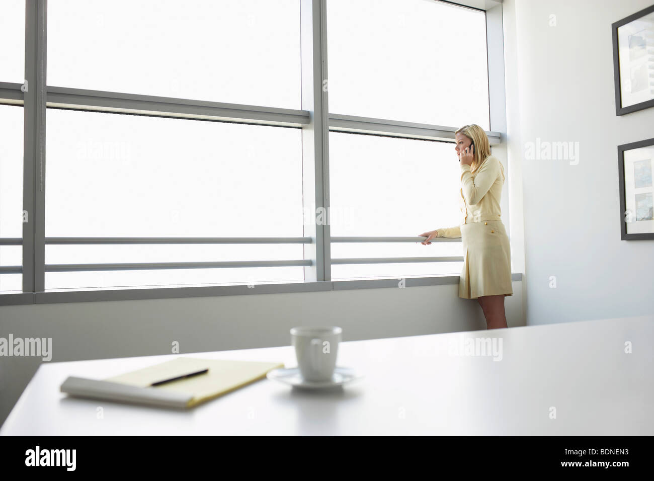 Business-Frau mit Handy stehende Fenster im Büro, Seitenansicht Stockfoto