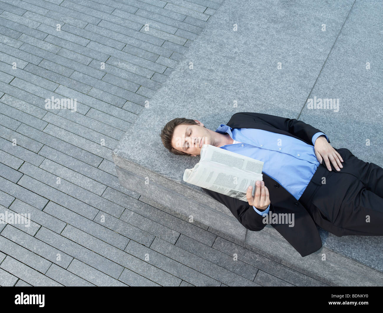 Junger Geschäftsmann liegen auf Wand auf Asphalt, lesen Zeitung, erhöht, Ansicht Stockfoto